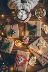 Woman drinking hot chocolate with marshmallows. Wooden table full of beautiful vintage Christmas presents. Top view