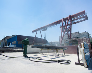 Fototapeta premium factory for cleaning of metal by sandblasting. a worker cleans the metal by sandblasting