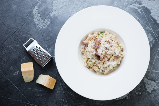Risotto with chanterelle mushrooms and parmesan served in a white plate. View from above on a grey stone background