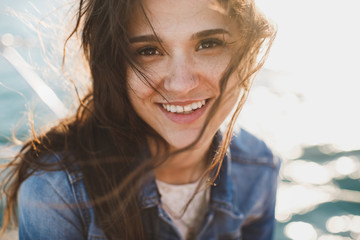 Beautiful young woman at the ocean standing against a turquoise blue sea with her hair blowing in the breeze