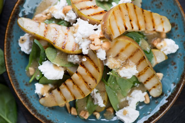 Salad with fresh spinach leaves, grilled pear slices, feta cheese and nuts, view from above, close-up