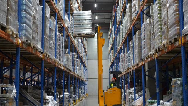 man on the loader in the warehouse lowers the container from the third level to the second