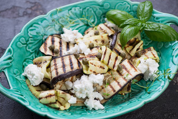 Grilled slices of eggplants and zucchini with olive oil, capers and cheese, closeup, studio shot