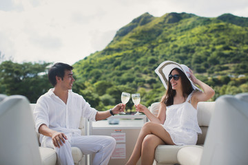 Fototapeta premium Smiling young couple holding glasses with champagne and looking at each other while sitting on the board of yacht
