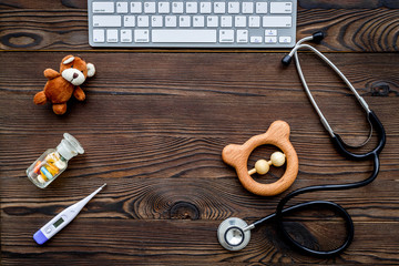 Pediatrician. Stethoscope, thermometer, pills, toys near keyboard on dark wooden background top view copyspace
