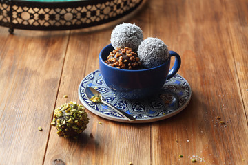 Fototapeta na wymiar Vegan Chocolate Cake Pops sprinkled with pistachios, walnuts and coconut, in blue cup, on wooden background.