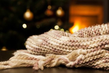 warm knitted scarf on chair, christmas tree and burning fireplace in the background - hygge concept