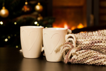 two tea mugs, knitted scarf and christmas tree and fireplace in the background - hygge concept