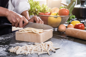 female housewife making homemade pasta with flour and eggs over table in kitchen