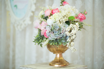 A beautiful bouquet of flowers in a vase of gold color on a wooden pallet