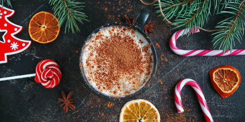 Obraz na płótnie Canvas Christmas hot chocolate in a black cup with caramelized oranges, fir branches and candy cane on dark background, Banner