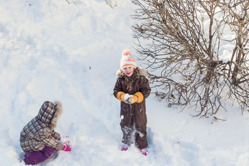 Beautiful little girl playing in freshly fallen snow in winter park with her friend