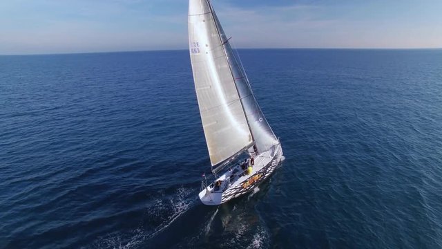 Beautiful epic drone aerial footage on warm sunny day at blue open ocean at sea, white professional yacht during racing competition, full open sails, spinnaker and mainsail at mast