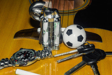 Wrist watch, cigarette, lighter, keychain with keys and acoustic guitar in the background