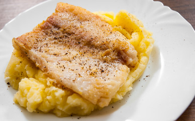 Fried fish fillet of cod with mashed potato in white plate on wooden background.