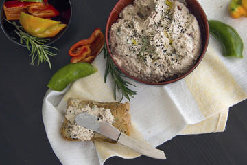 Dip from cottage cheese with sun dried tomatoes, tuna, parsley greens sprinkled with grains of black cumin, served with toast from grain bread on a black background