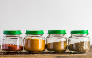 Spices and seasoning containers, glass pots and bowls in a row, on a wooden surface and white background