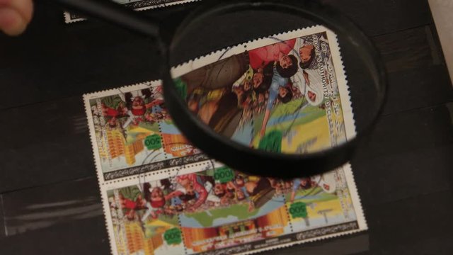 Collector philatelist leafs through the album with a collection of postage stamps and looks  at the stamps through a magnifying glass