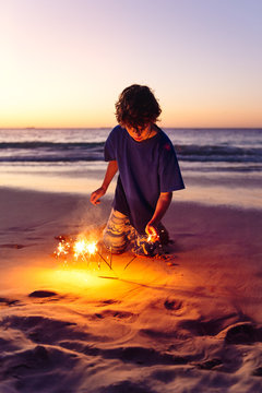 Boy lighting sparklers in the sand at the beach at night