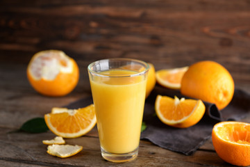 Glass of fresh juice and oranges on wooden background
