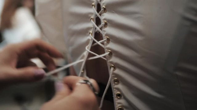 Stylist helps to tighten the corset of a historical dress on woman. 18th century look. Hands close-up. slow motion