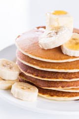 pancakes with butter, banana and honey on a white plate and against a white background