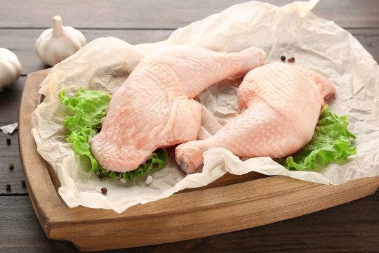 Board with raw chicken legs on wooden background
