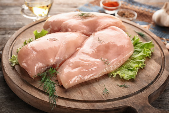 Wooden board with raw chicken fillet on table, closeup
