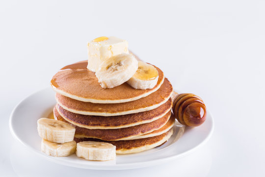 pancakes with butter, banana and honey on a white plate and against a white background