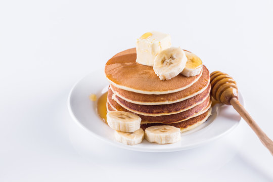 pancakes with butter, banana and honey on a white plate and against a white background