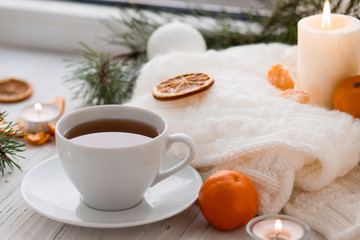 Fototapeta na wymiar Winter breakfast. Tangerine and a cup of tea. Tree and the candles on the windowsill. Christmas morning 