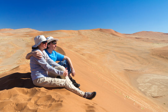 African vacation holiday, tourists sitting on dune, couple in Namib desert dunes and lanscape, travel in Namibia, Africa
