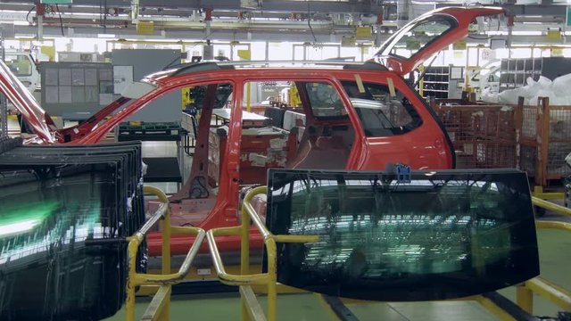 car body is moving slowly on a conveyor in a factory shop, windows for automobiles are lying
