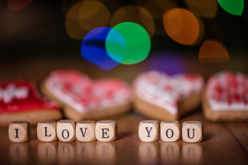 i love you spelled out of wooden blocks with icing decorated heart shape cookies in a background