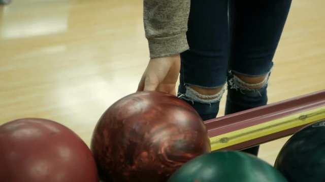 Close-up of varicolored bowling balls, woman takes ball