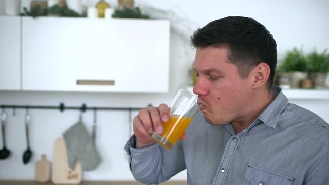 Attractive young man drinking orange juice in a kitchen. Healthy lifestyle. slow-motion