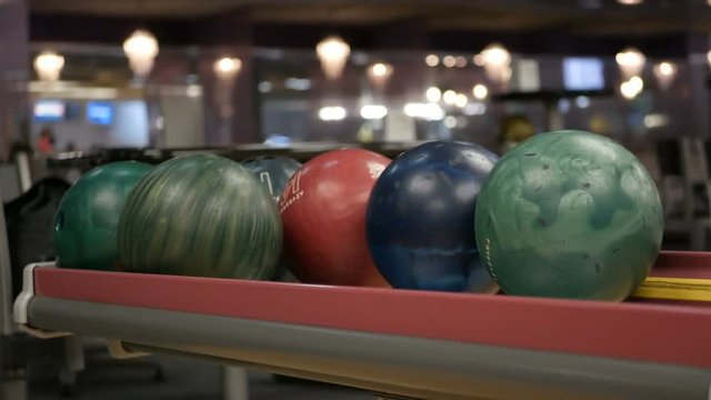 Close-up of varicolored bowling balls, woman takes ball