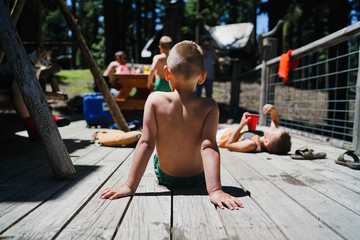 Rear view of boy sitting on a wooden floor during summer