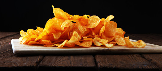 Crispy potato chips. Paprika chips on wooden background.