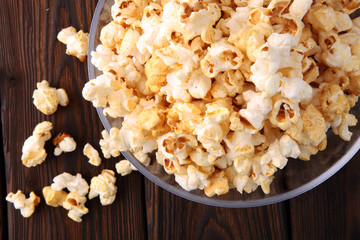 Glass bowl with popcorn on brown wooden background