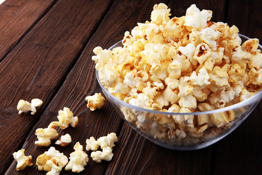 Glass bowl with popcorn on brown wooden background