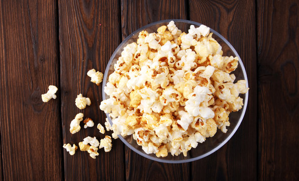 Glass bowl with popcorn on brown wooden background