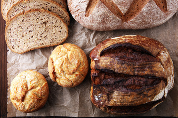 Different kinds of bread and bread rolls on brown wooden table. Kitchen or bakery poster design.