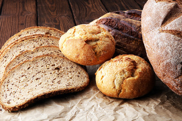 Different kinds of bread and bread rolls on brown wooden table. Kitchen or bakery poster design.