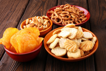 Salty snacks. Pretzels, chips, crackers on brown wooden background