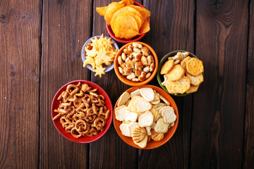 Salty snacks. Pretzels, chips, crackers on brown wooden background