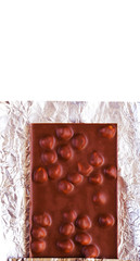 Dark chocolate bar with hazelnuts on a foil isolated on white, top view, vertical image