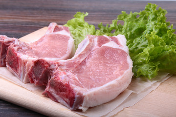 Fototapeta premium Raw pork steak with spices Leaves lettuce on wooden cutting board. Ready for cooking.