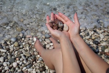Woman holds color stones sitting on the beach