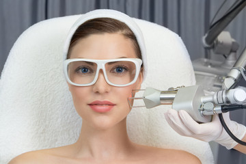 Therapist beautician makes a  laser rejuvenation for the model by  apparatus  in a beauty salon.